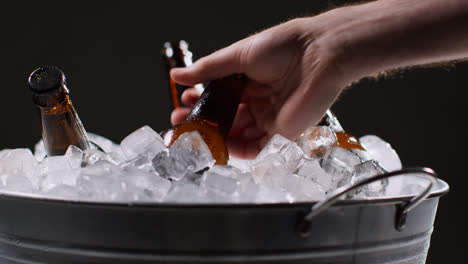 Nahaufnahme-Einer-Person,-Die-Eine-Gekühlte-Glasflasche-Mit-Kaltem-Bier-Oder-Alkoholfreien-Getränken-Aus-Einem-Mit-Eis-Gefüllten-Eimer-Vor-Schwarzem-Hintergrund-Nimmt